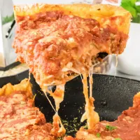 A slice of pizza dripping with melted cheese being lifted out of a cast-iron pan holding the rest of the pizza - Hostess At Heart