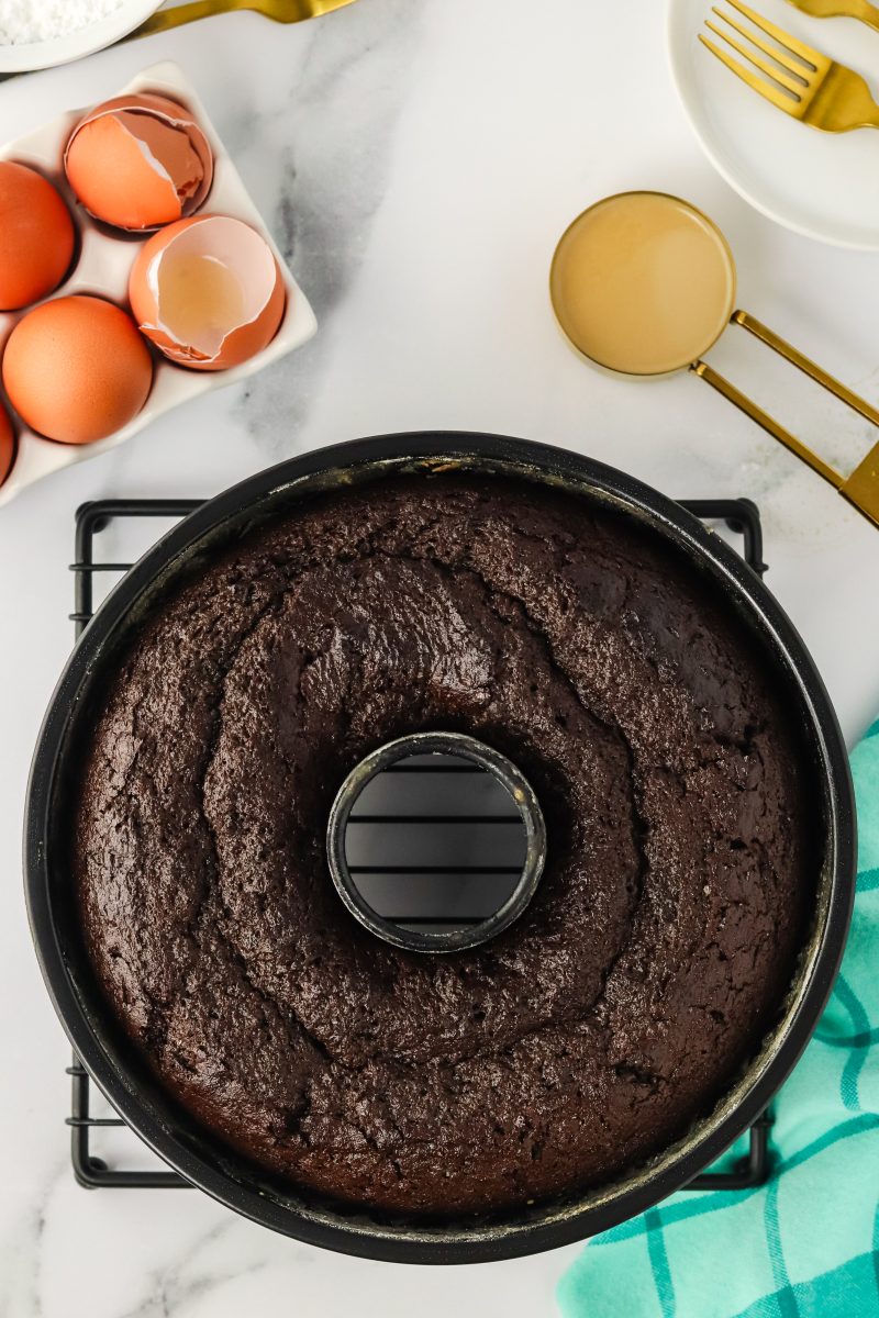 Top down view of a baked dark chocolate bundt cake sitting on a cooling rack. Hostess At Heart