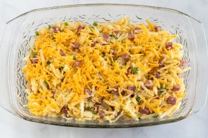 A baking dish filled with shredded potatoes, cheese, diced corned beef, onions, and green peppers - Hostess At Heart