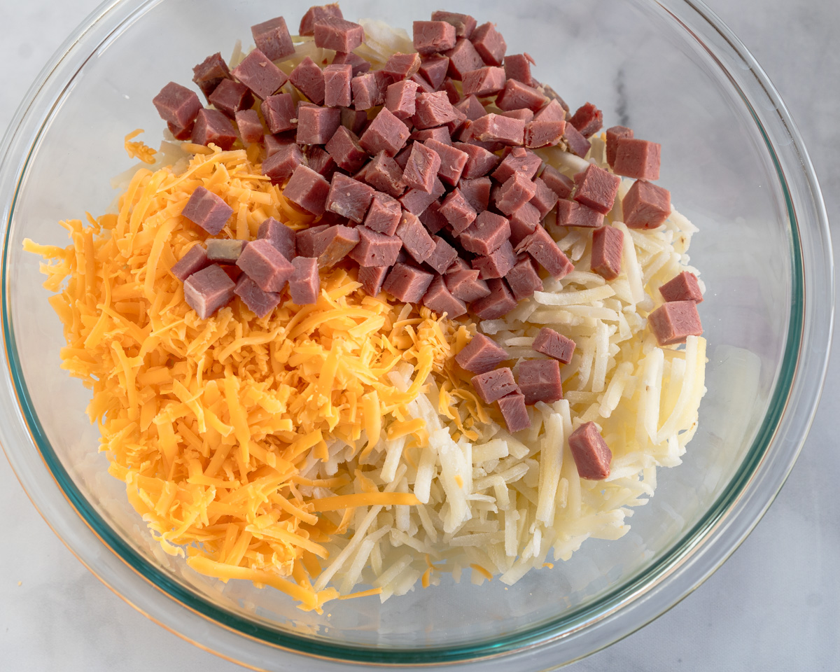 A mixing bowl filled with diced corned beef and shredded cheese and potatoes - Hostess At Heart
