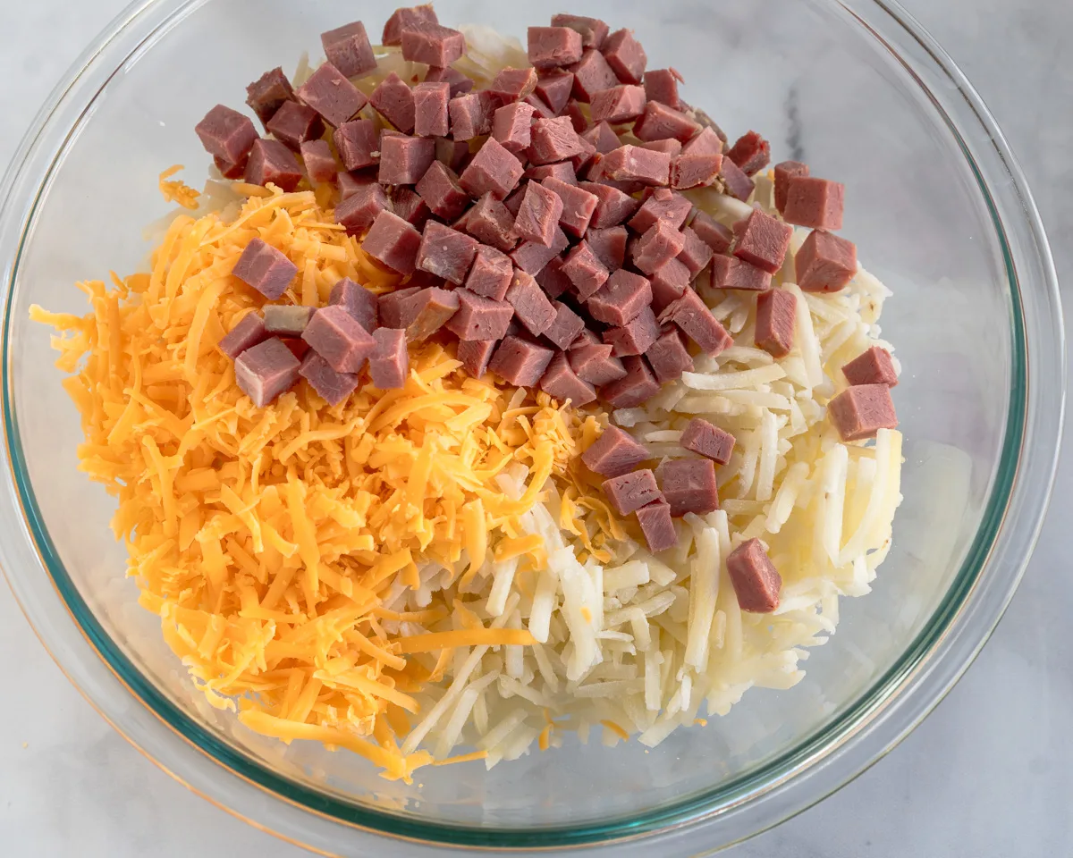 A mixing bowl filled with diced corned beef and shredded cheese and potatoes - Hostess At Heart