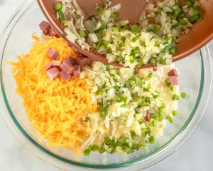 A mixing bowl filled with diced corned beef, onions, green peppers, shredded cheese and potatoes - Hostess At Heart