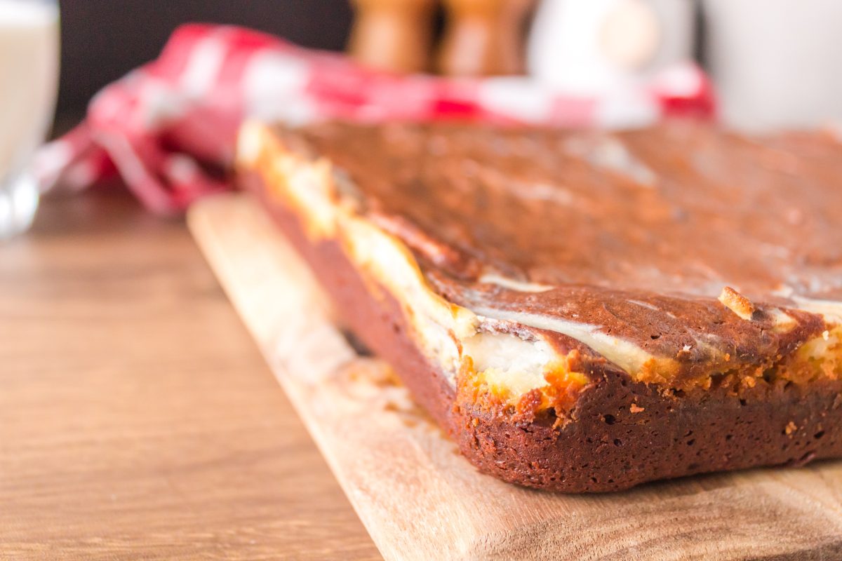 A slab of a baked Chocolate Cream Cheese Brownie sitting on a cutting board - Hostess At Heart