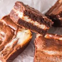 Close up of three chocolate swirled cream cheese brownies with one propped up showing the layers - Hostess At Heart