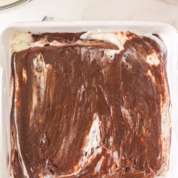 Baking dish filled with brownie batter thats filled with a cream cheese mixture - Hostess At Heart