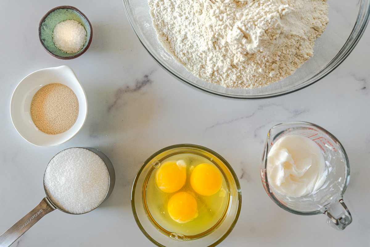 Top down view of the ingredients used to make Medianoche Bread Rolls including flour, lard, sugar, eggs, yeast, and salt.