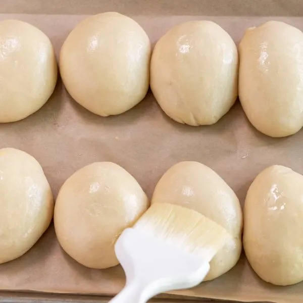 Egg wash being applied using a pastry brush over the top of shaped bread rolls - Hostess At Heart