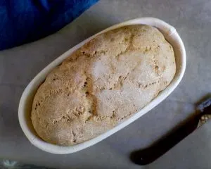 A loaf of risen sourdough pumpernickel bread sitting in a banneton basket - Hostess At Heart