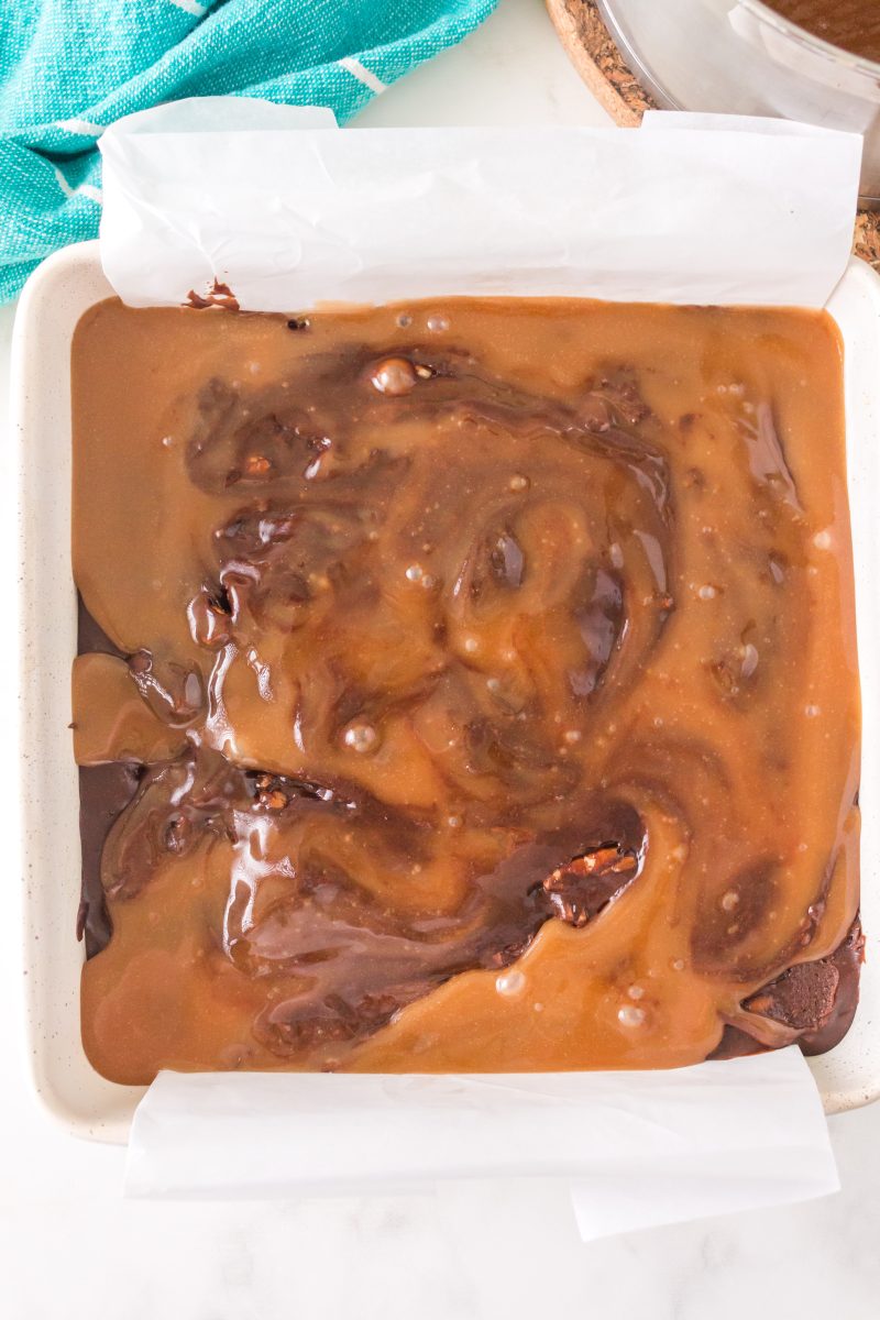 Top down view of brownie pan with brownie batter on bottom and caramel sauce on top.