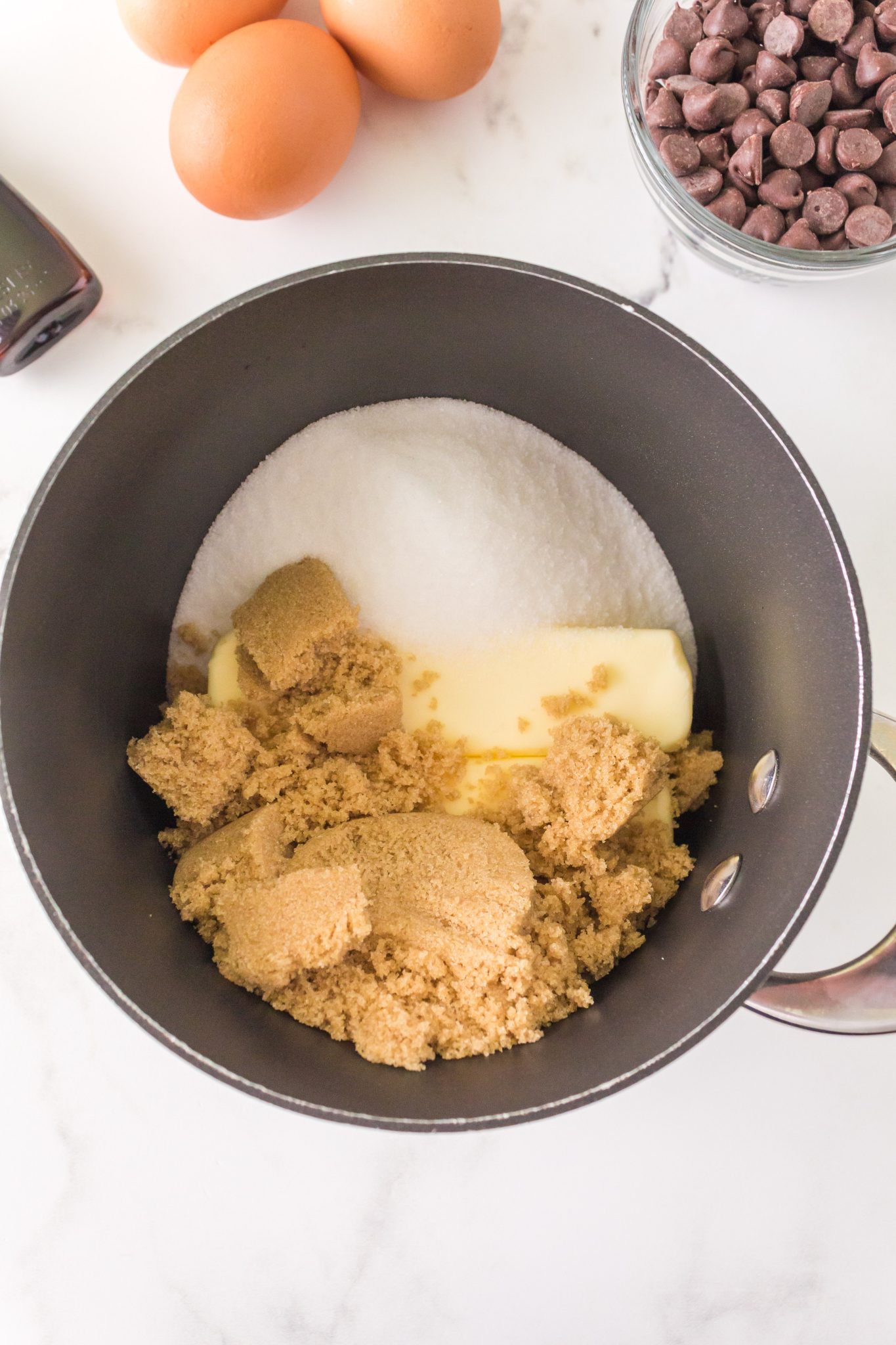 Top down view of a saucepan filled with a stick of butter, brown sugar, and white sugar.
