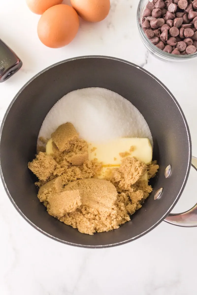 Top down view of a saucepan filled with a stick of butter, brown sugar, and white sugar.