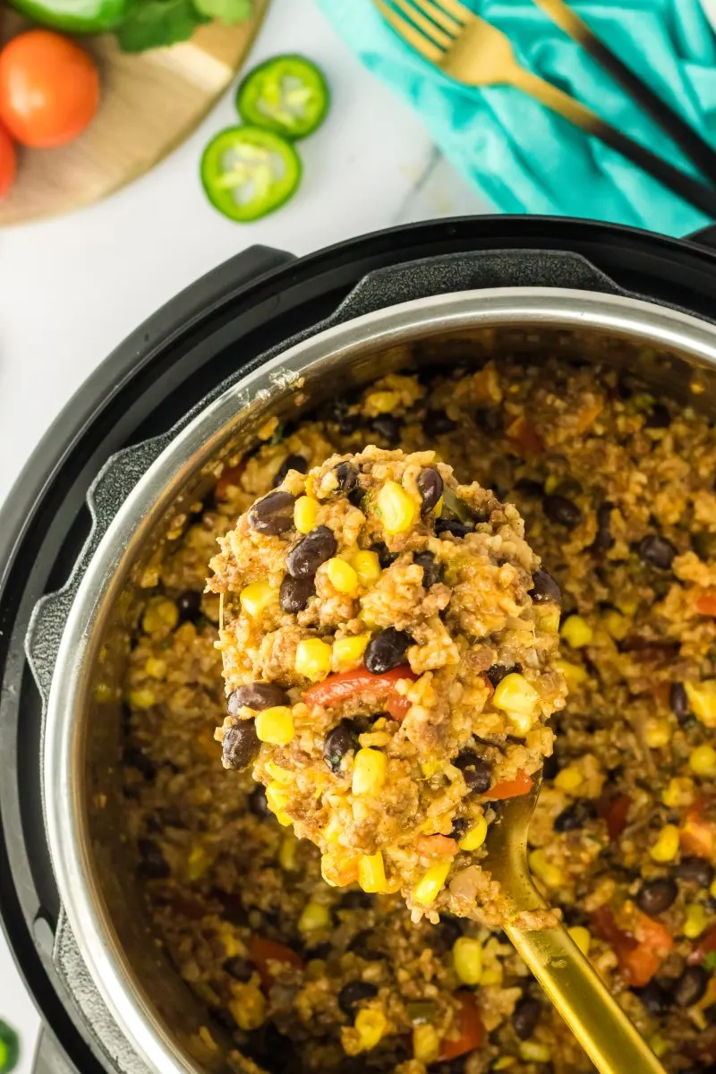 A large serving spoon filled with homemade dirty rice hovering over an instant pot - Hostess At Heart