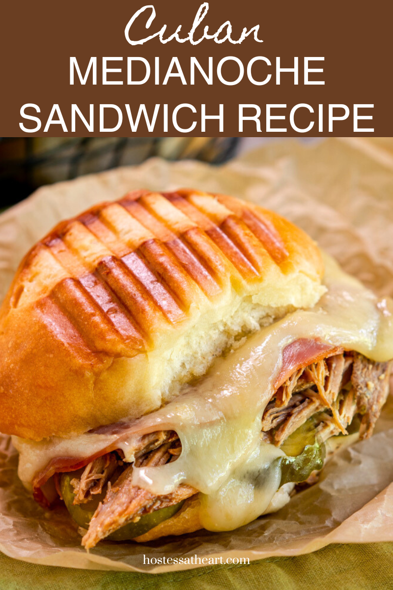 Image for Pinterest a sideview of a Medianoche Cuban Sandwich oozing with cheese, shredded pork and pickles under a panini pressed bread roll - Hostess At Heart