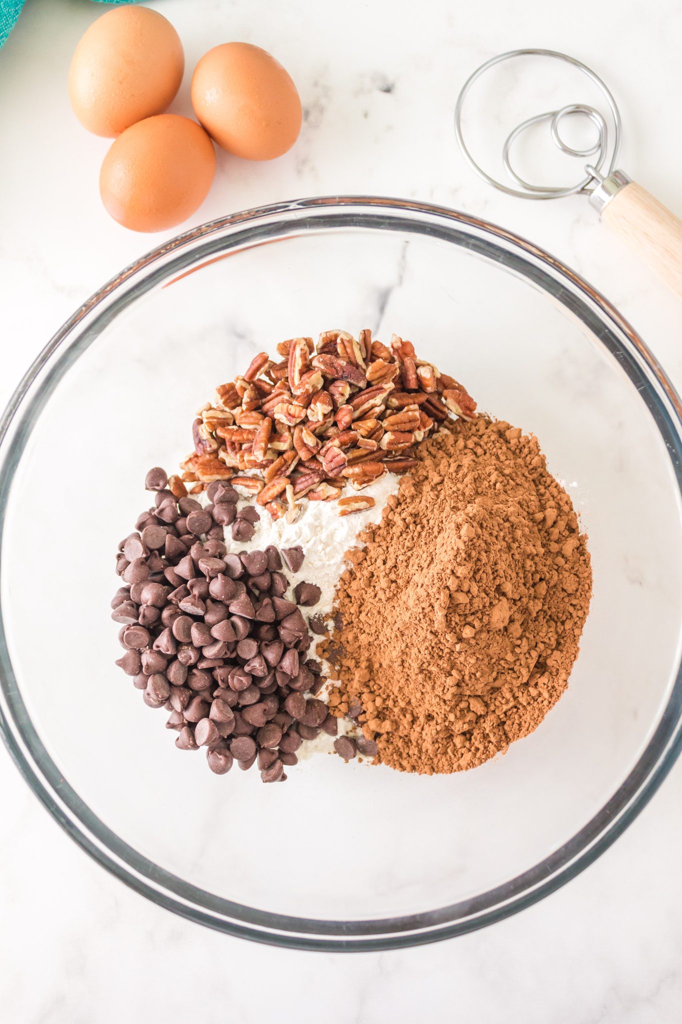 A mixing bowl filled with chocolate chips, cocoa, flour, and chopped pecans - Hostess At Heart