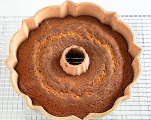 A baked rum bundt cake sitting in the pan over a cooling rack - Hostess At Heart