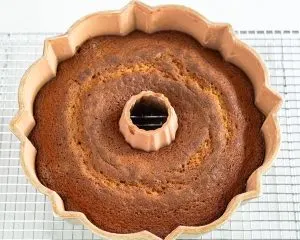 A baked rum bundt cake sitting in the pan over a cooling rack - Hostess At Heart