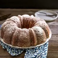 Sideview of a Cuban Rum Bundt Cake dusted with powdered sugar on a serving platter. Hostess At Heart