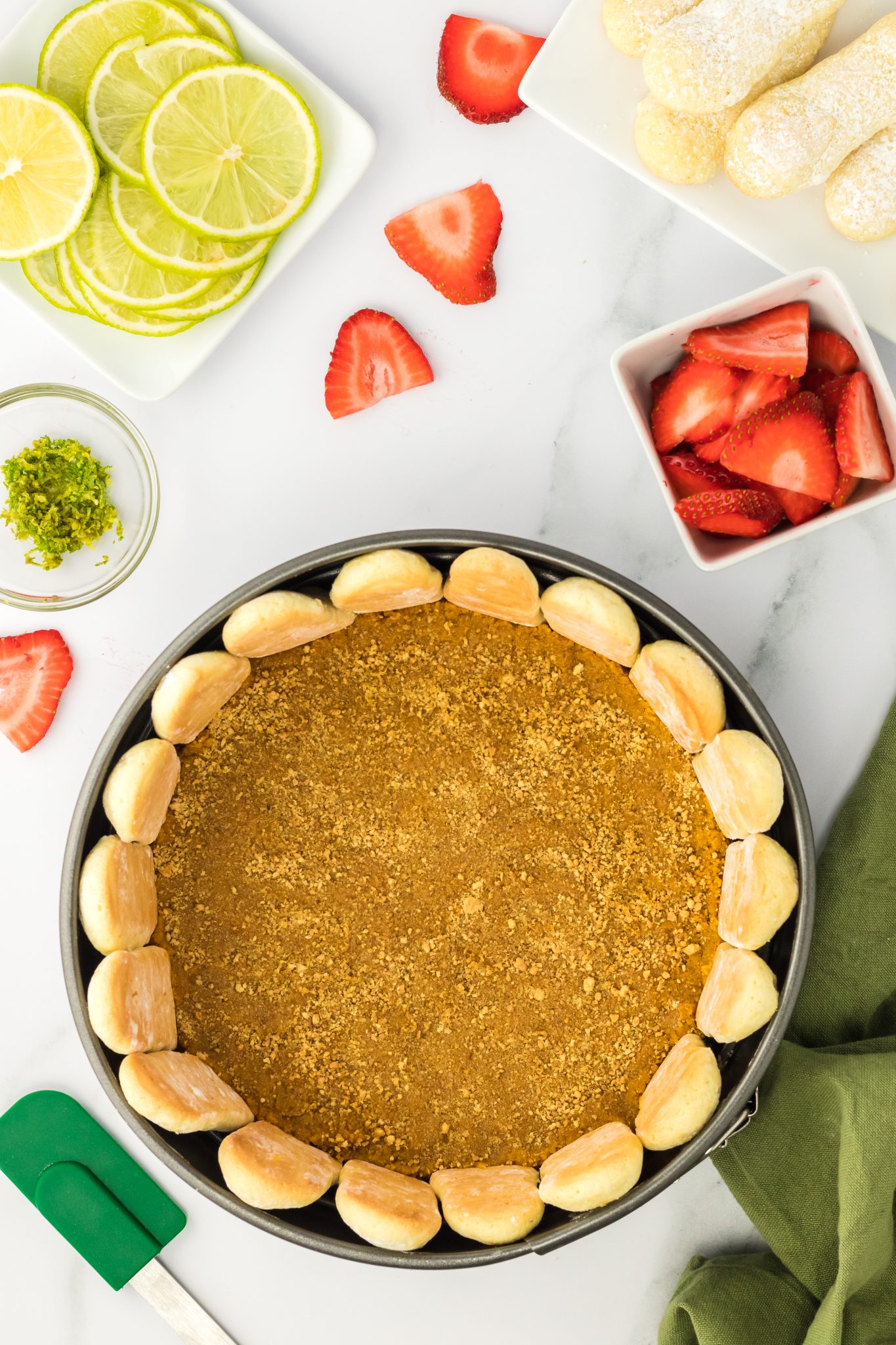 top down view of graham cracker crust formed in the bottom of a springform pan with ladyfingers around the edge.
