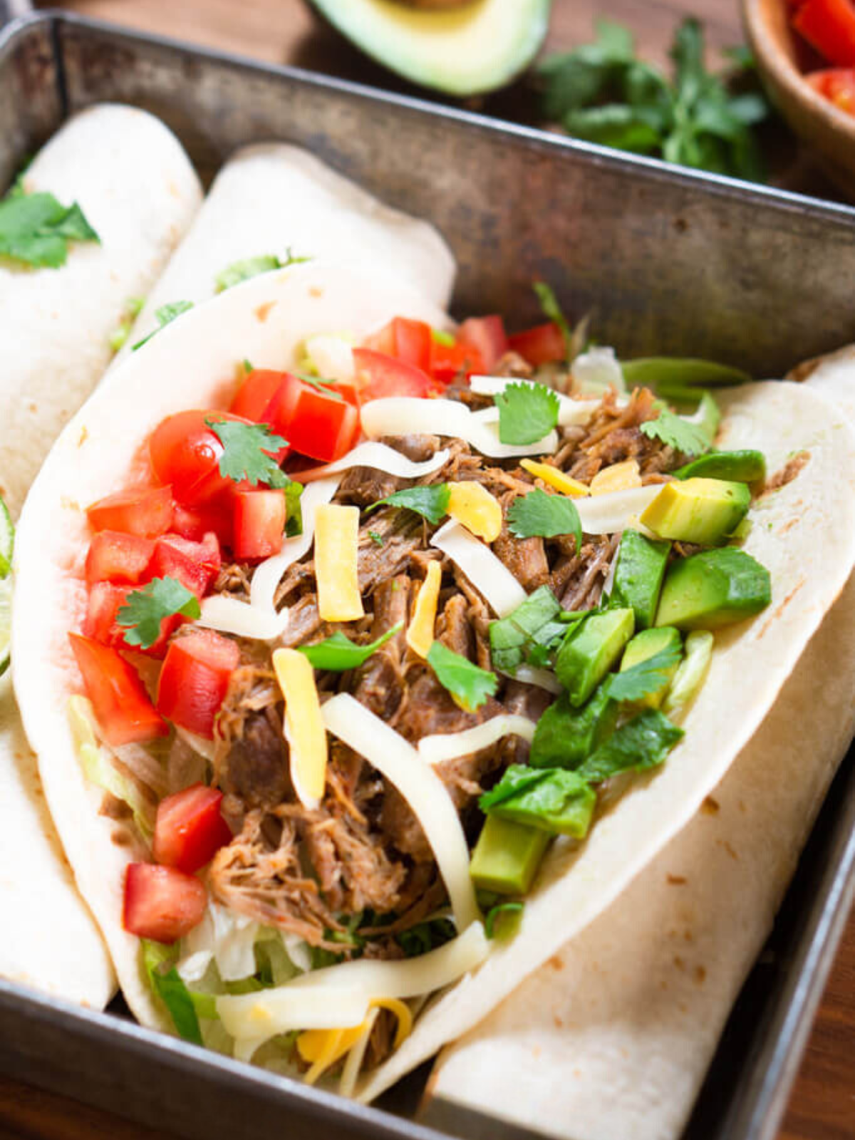 Angled view of a soft taco shell filled with shredded pork avocado, tomatoes, and shredded cheese.