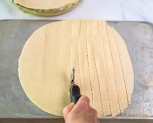 Rolled pie dough on a baking sheet being cut into strips with a ravioli cutter to make a lattice crust top - Hostess At Heart