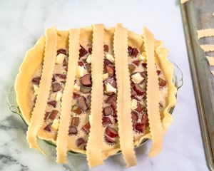 The first pie dough strips running vertically over a filled pie in order to make a lattice crust - Hostess At Heart