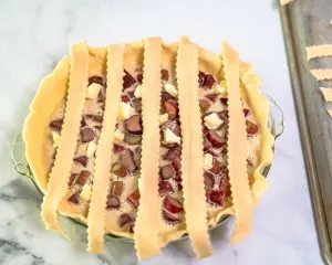 The first pie dough strips running vertically over a filled pie in order to make a lattice crust - Hostess At Heart