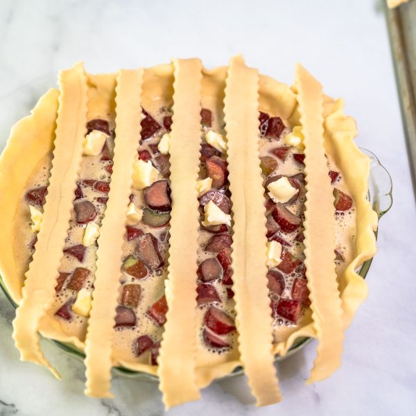 The first pie dough strips running vertically over a filled pie in order to make a lattice crust - Hostess At Heart