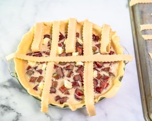 The first horizontal strip of pie dough crossed over a pie to weave with vertical strips to make a lattice crust. Hostess At Heart