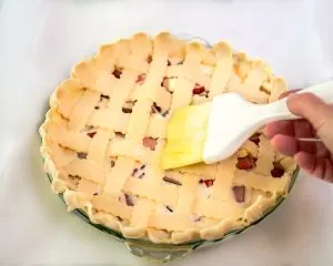 A lattice pie crust being brushed with egg wash before baking - Hostess At Heart