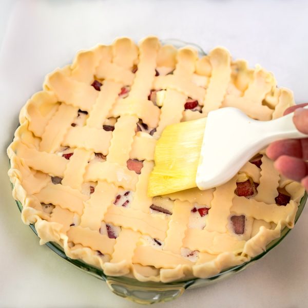 A lattice pie crust being brushed with egg wash before baking - Hostess At Heart