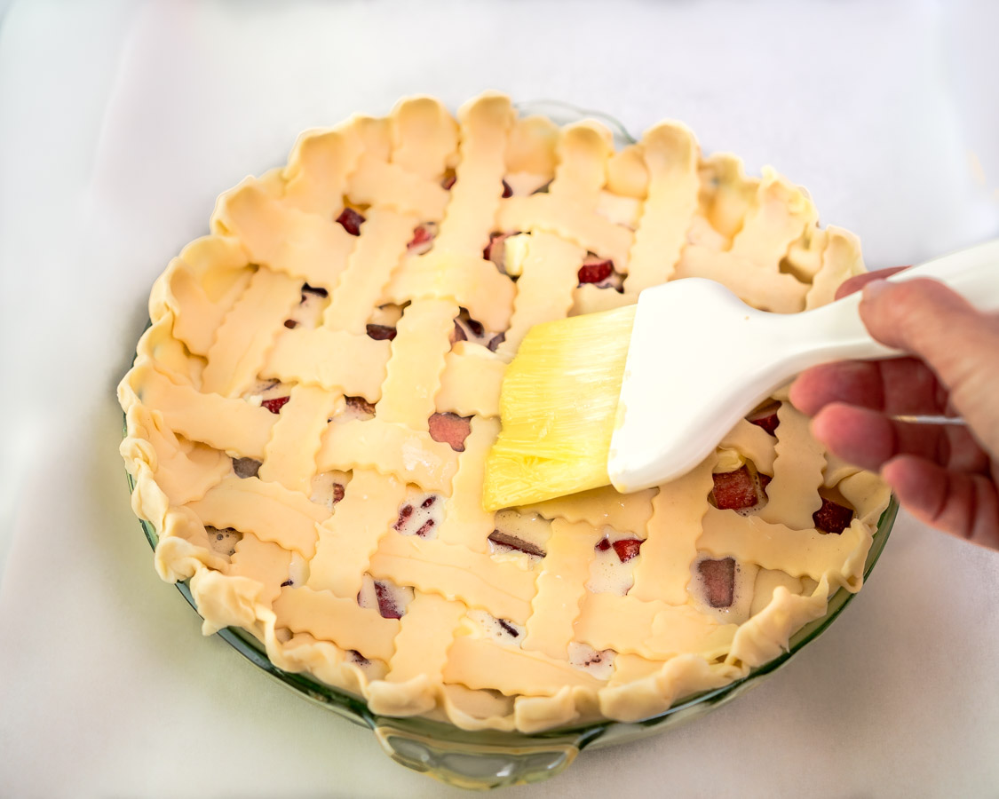 A lattice pie crust being brushed with egg wash before baking- Hostess At Heart