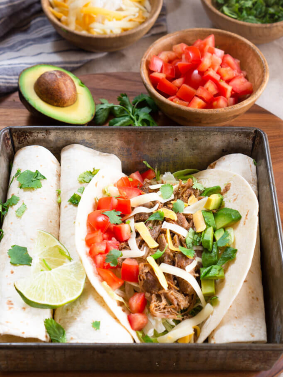 Top down view of a soft shell instant pot pulled pork taco garnished with diced tomatoes, avocados, and shredded cheese. Hostess At Heart