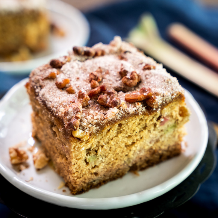 Sideview of a moist cake with fresh rhubarb and topped with a crusty sugar, cinnamon, and walnut topping. Hostess At Heart