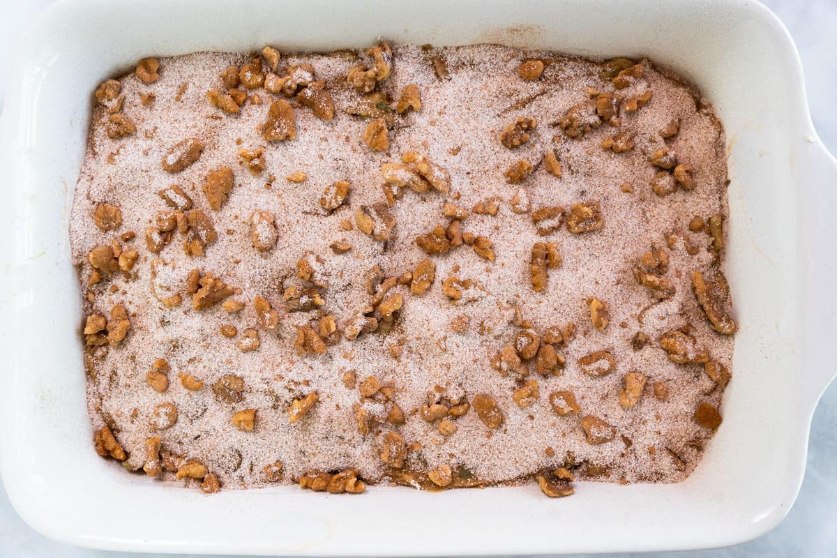 Cake pan filled with a batter topped with sugar, cinnamon and walnuts - Hostess At Heart