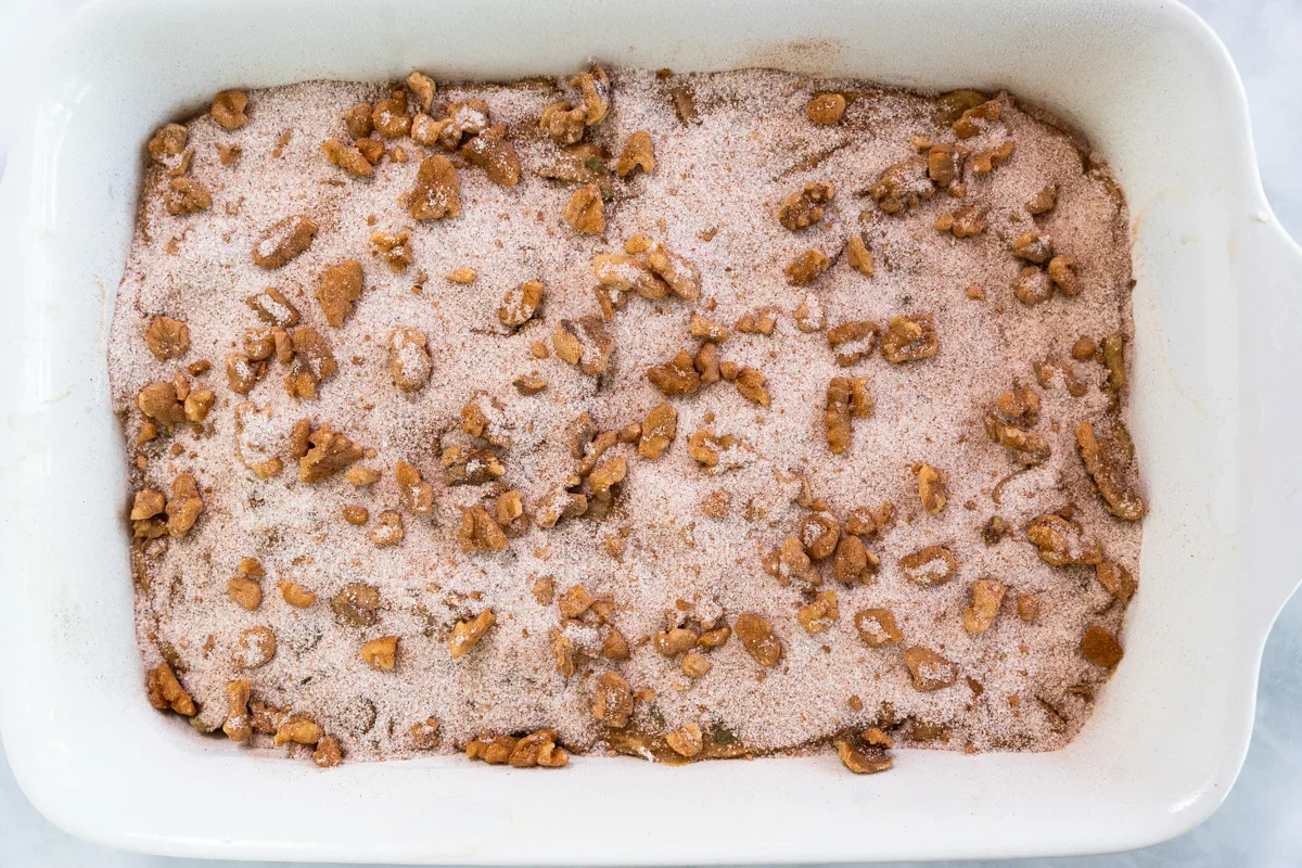 Cake pan filled with a batter topped with sugar, cinnamon and walnuts - Hostess At Heart
