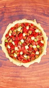 Top down view of a pie filled with strawberries and rhubarb filling, dotted with pieces of butter - Hostess At Heart