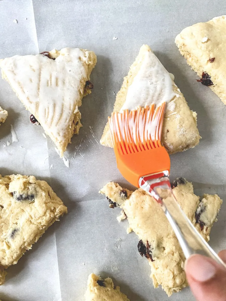 A pastry brush applying cream to an unbaked cherry scone wedge - Hostess At Heart