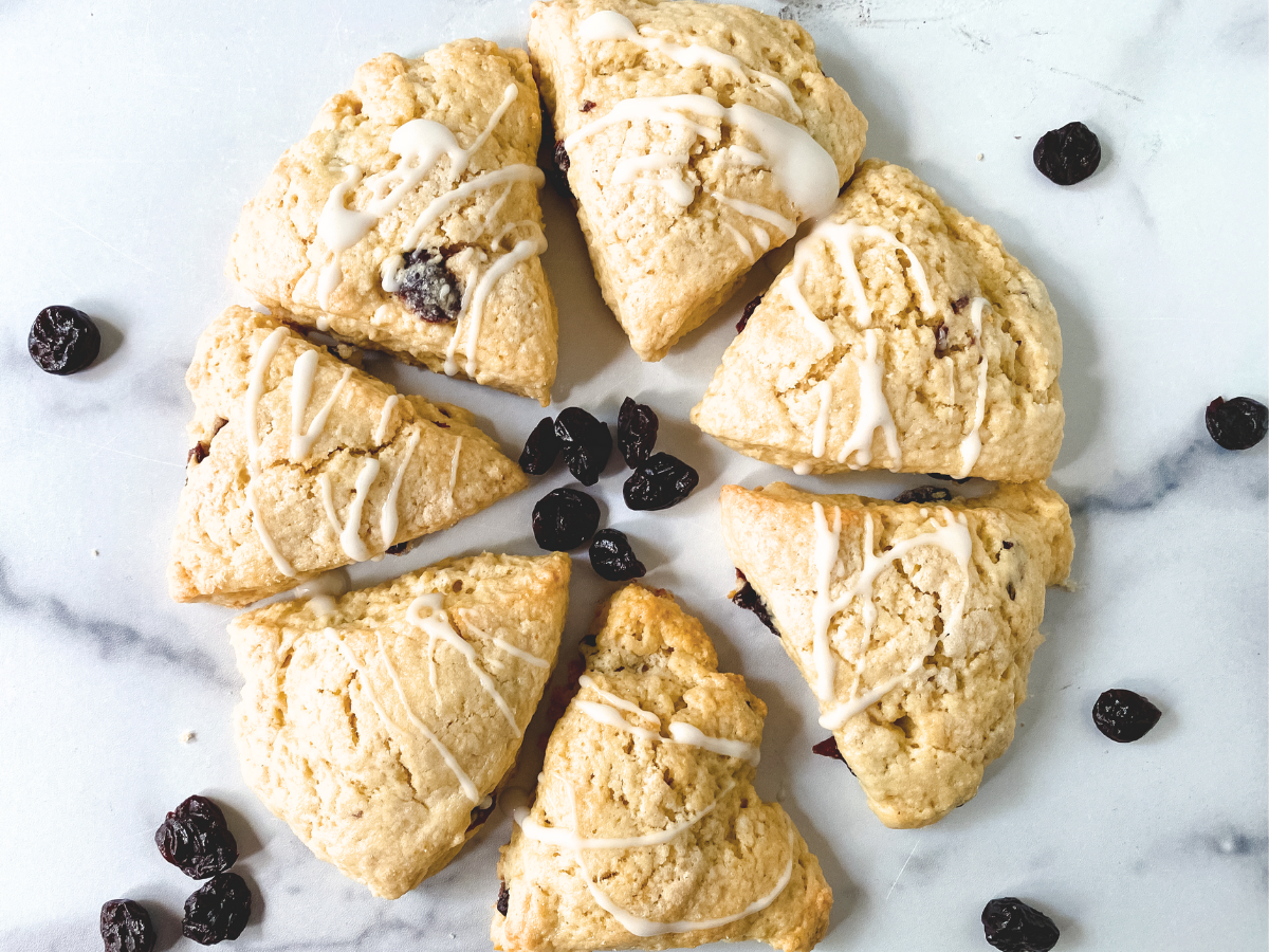 Top down view of baked scones that were shaped into a circle and cut into wedges. They're garnished with a vanilla drizzle and dried cherries - Hostess At Heart