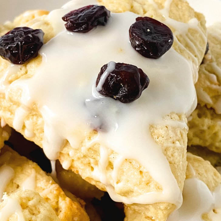 Close up view of a cherry scone wedge garnished with vanilla glaze and dried cherries - Hostess At Heart