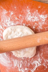 A rolling pin rolling homemade pizza crust on a floured work surface - Hostess At Heart