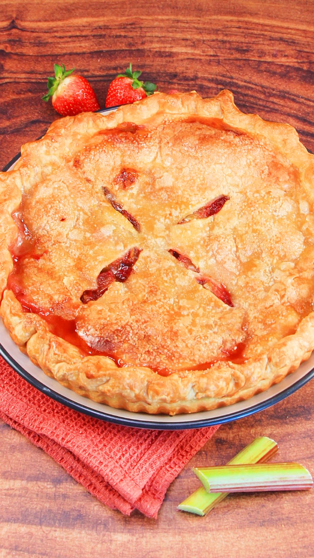 Sideview of a baked golden brown pie with strawberry and rhubarb juice bubbled around the edges - Hostess At Heart