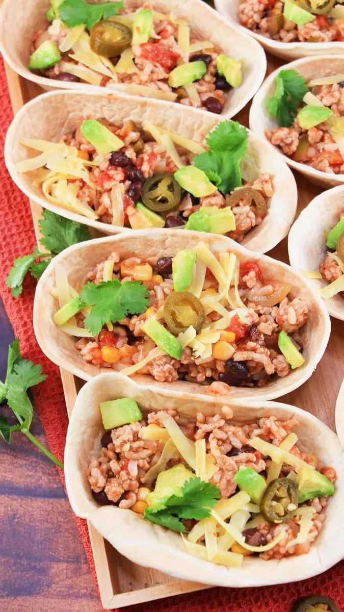 Close up image of tacos filled with ground pork and rice garnished with cheese, fresh cilantro and jalapeno slices,