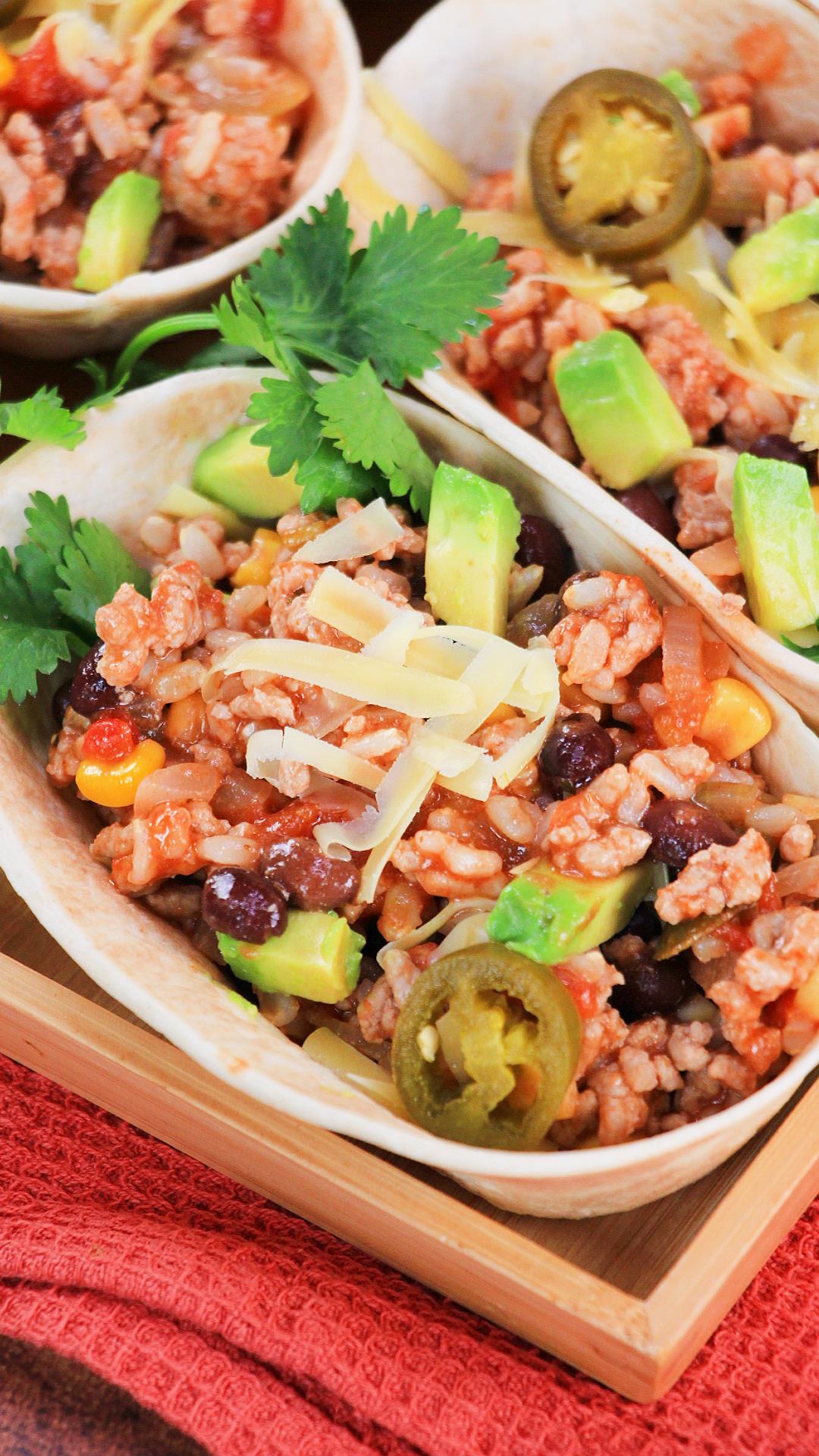 Closeup view of a taco bowl filled with green chili filling consisting of browned ground pork, rice, beans, corn and spices then garnished with cilantro, jalapeno, and cheese - Hostess At Heart
