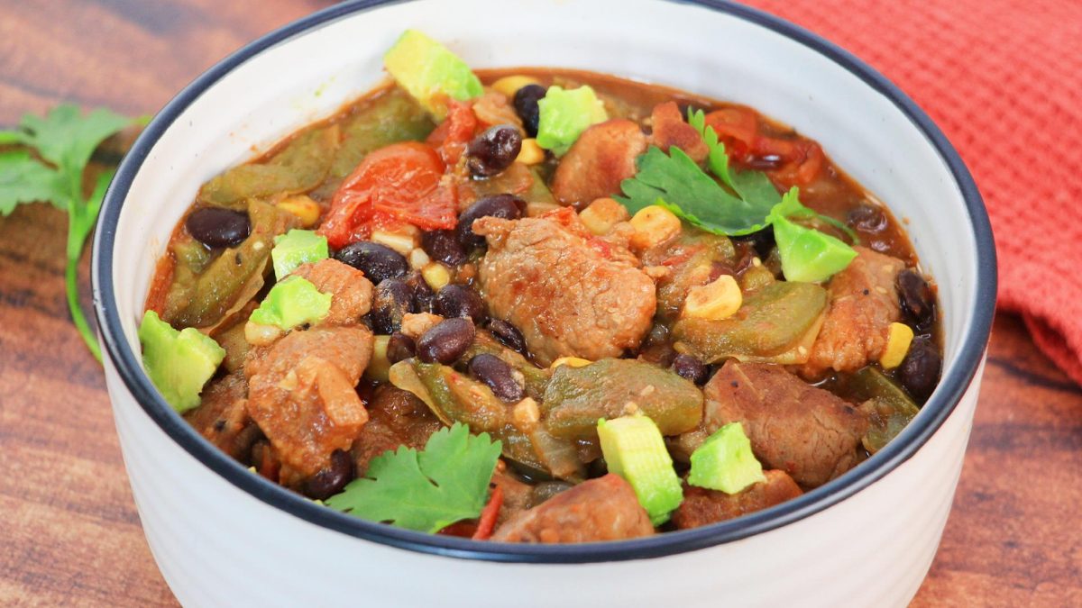 A spicy green chili pepper stew filled with chunks of pork, black beans, tomatoes, corn, and topped with cilantro and avocado.