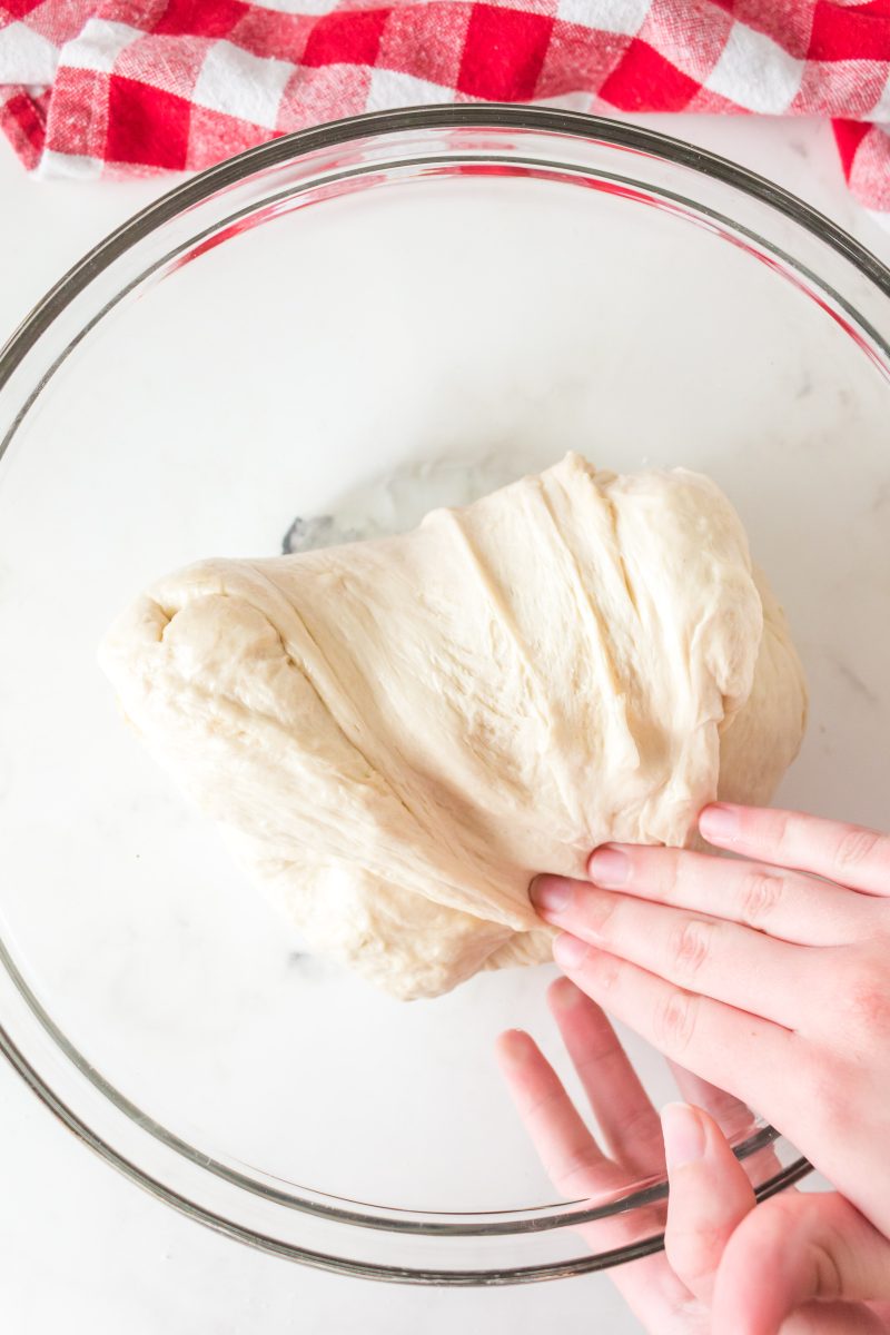 A hand folding homemade pizza dough over onto itself to make sourdough pizza crust - Hostess At Heart