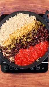 Top down view of a skillet filled with black beans, tomatoes, corn, and green chilies over ground pork. Hostess At Heart