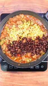 Top down view of corn and black beans added to a skillet of pork green chili stew. Hostess A Heart