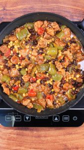 Green Chile Pork stew in a skillet with black beans, corn, and tomatoes. Hostess At Heart