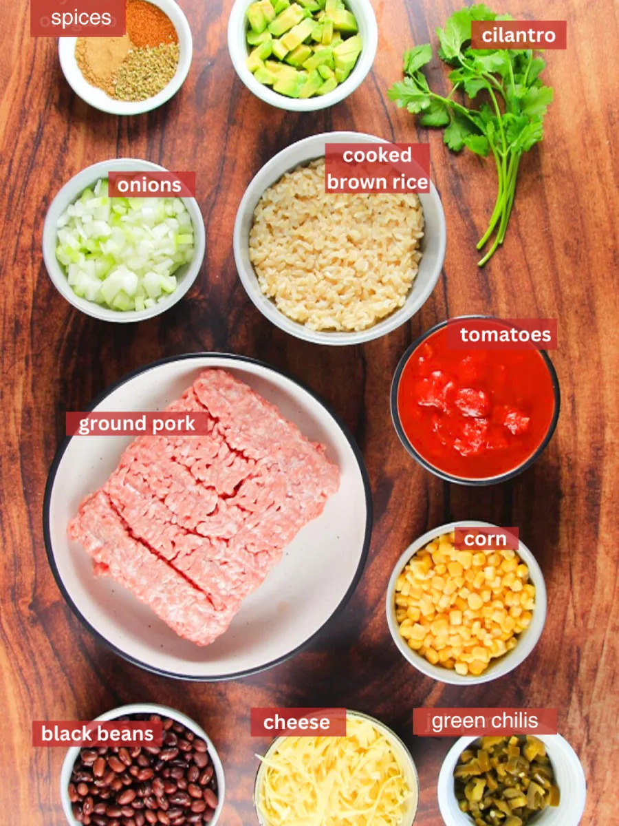 Ingredients used to make Green Chili Pork including Ground Pork, cheese, black beans, green chilis, corn, tomatoes, rice, and spices. Garnishes include avocados and fresh cilantro - Hostess At Heart