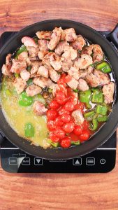 Top down view of a skillet filled with canned tomatoes, browned pork, diced poblano peppers, and pureed tomatillos - Hostess At Heart